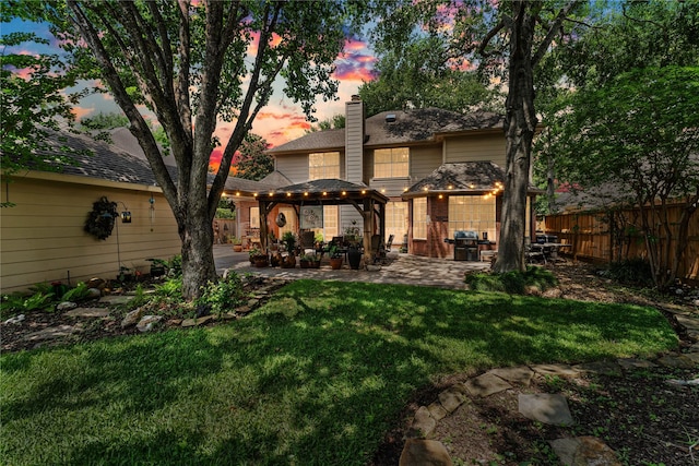 back of house at dusk featuring a yard, a patio area, a fenced backyard, and a chimney