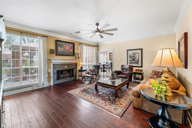 living room featuring a ceiling fan, a stone fireplace, crown molding, and plenty of natural light