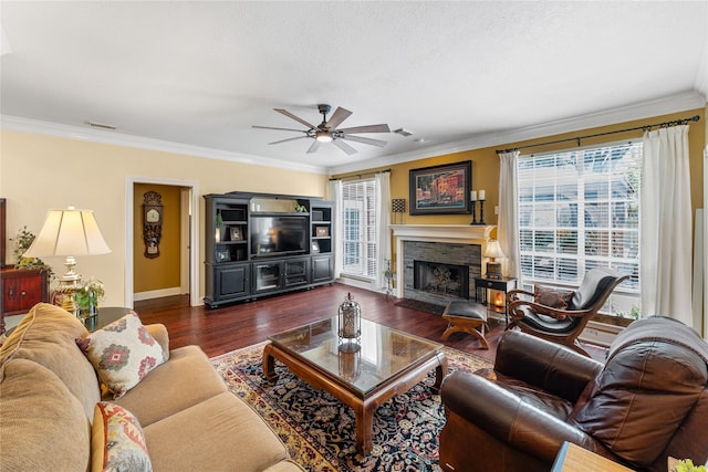 living area with a ceiling fan, a stone fireplace, and crown molding