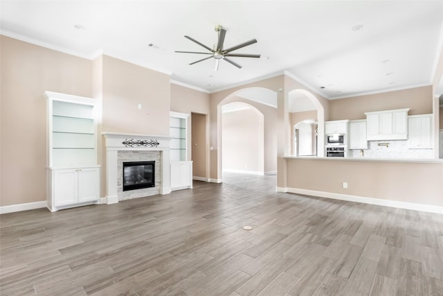 23446 Timbarra Glen Dr, New Caney, TX 77357 - unfurnished living room featuring arched walkways, a glass covered fireplace, light wood finished floors, ornamental molding, and a ceiling fan