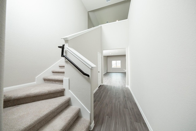 stairway with baseboards, a high ceiling, and wood finished floors