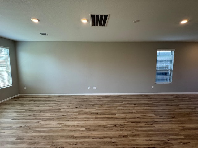 empty room featuring visible vents, wood finished floors, and a healthy amount of sunlight