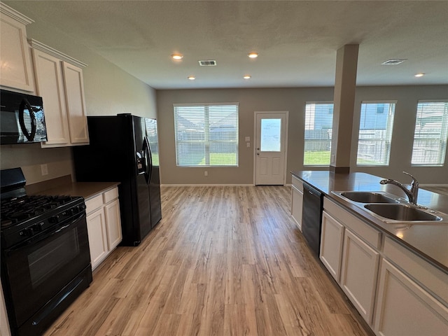 kitchen featuring black appliances, visible vents, a healthy amount of sunlight, light wood finished floors, and a sink