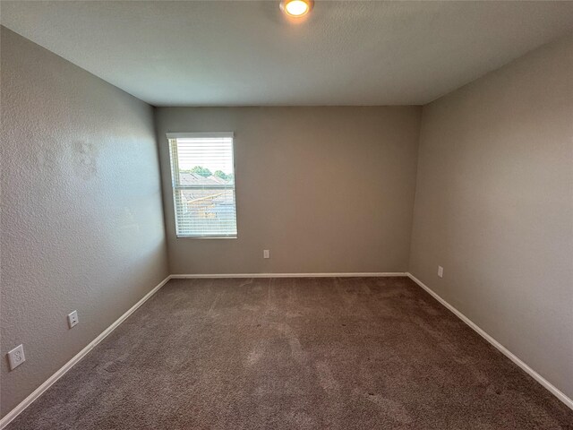 carpeted empty room featuring a textured wall and baseboards