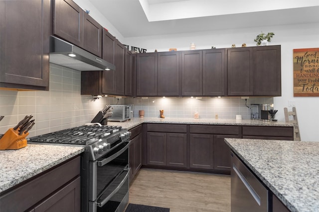 954 Golden Willow Ln, Conroe, TX 77304 - kitchen with stainless steel appliances, exhaust hood, light wood finished floors, decorative backsplash, and dark brown cabinetry