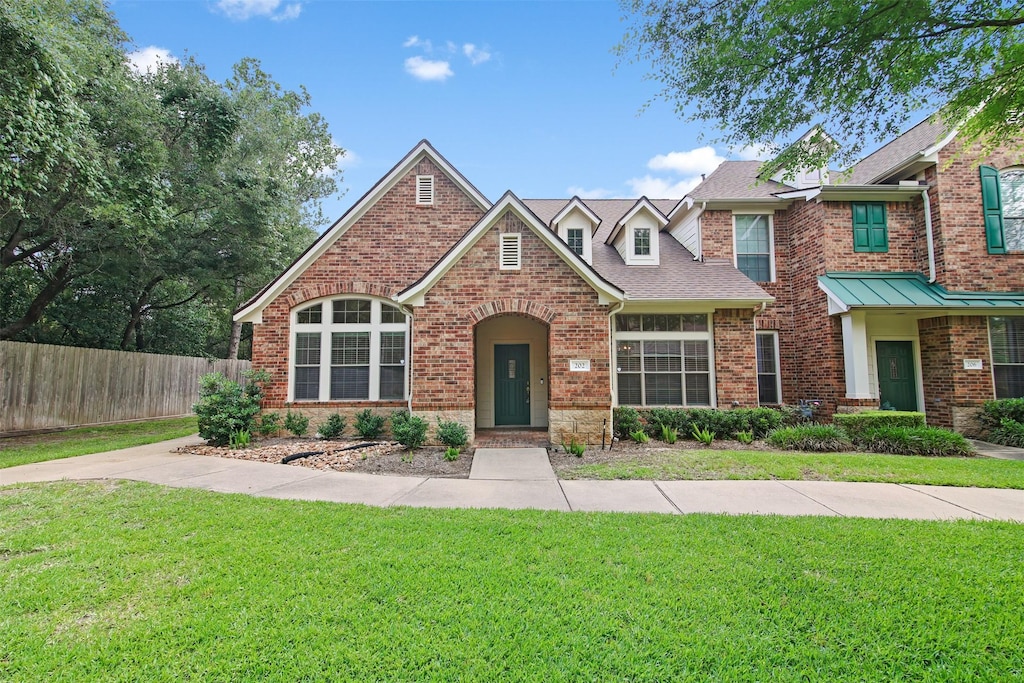 view of front of home with brick siding, a shingled roof, a front lawn, and fence