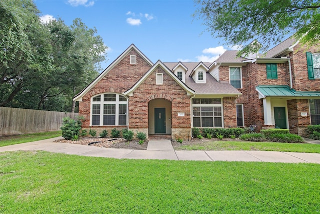 view of front of home with brick siding, a shingled roof, a front lawn, and fence