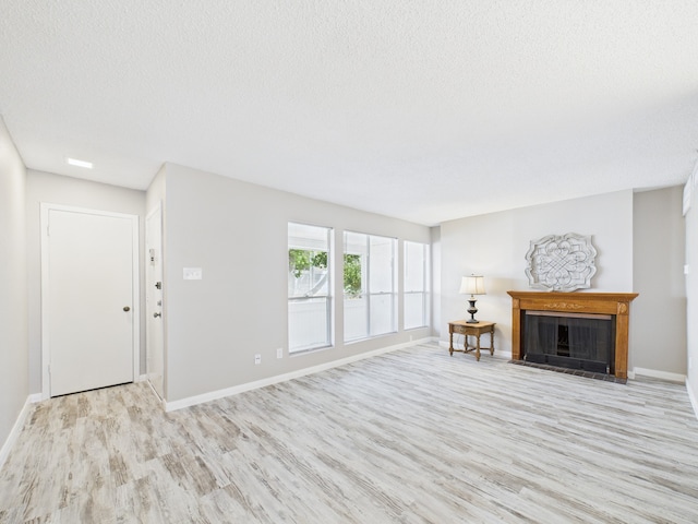 living area with baseboards, light wood finished floors, a fireplace with flush hearth, and a textured ceiling