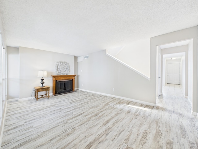 unfurnished living room with a fireplace with flush hearth, visible vents, light wood-type flooring, and baseboards