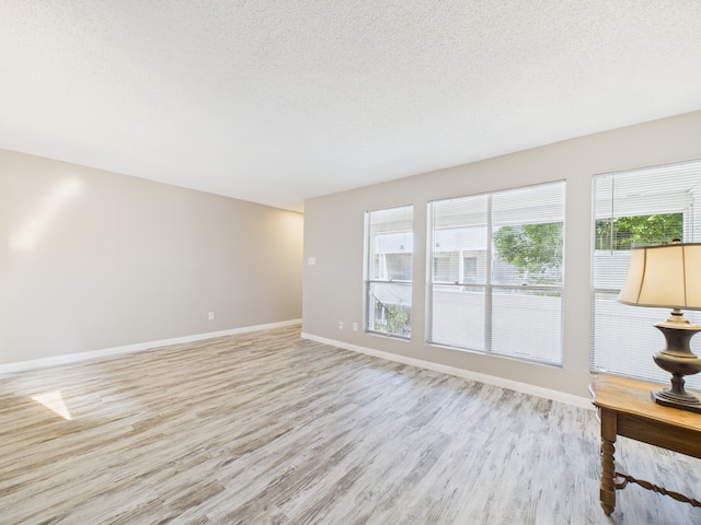 unfurnished living room with a textured ceiling, light wood finished floors, and baseboards