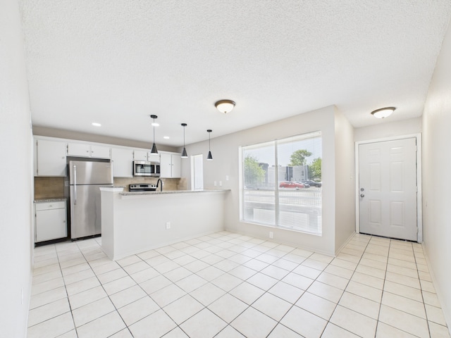 kitchen with light countertops, a peninsula, a textured ceiling, white cabinetry, and stainless steel appliances