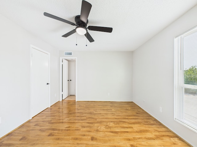 unfurnished room with light wood-type flooring, a ceiling fan, visible vents, and a textured ceiling