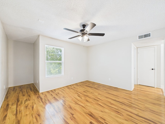 spare room with a textured ceiling, light wood finished floors, ceiling fan, and visible vents