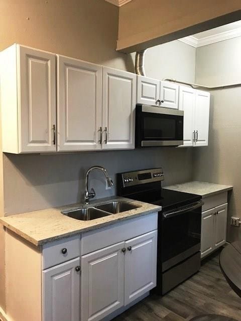 3522 Sampson St, Houston, TX 77004 - kitchen with dark wood finished floors, stainless steel appliances, ornamental molding, a sink, and white cabinetry