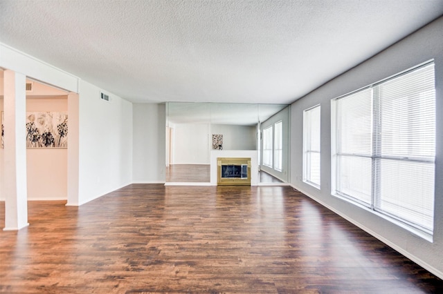 unfurnished living room with a glass covered fireplace, baseboards, a textured ceiling, visible vents, and dark wood finished floors