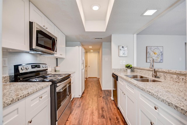 kitchen with light stone countertops, light wood-style flooring, white cabinets, appliances with stainless steel finishes, and a sink