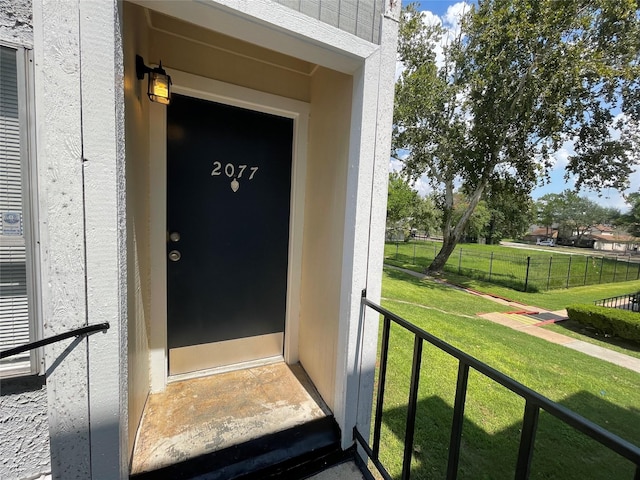 entrance to property featuring fence and a lawn