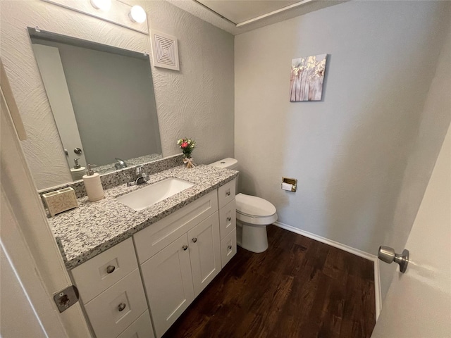 half bath featuring vanity, baseboards, toilet, and wood finished floors