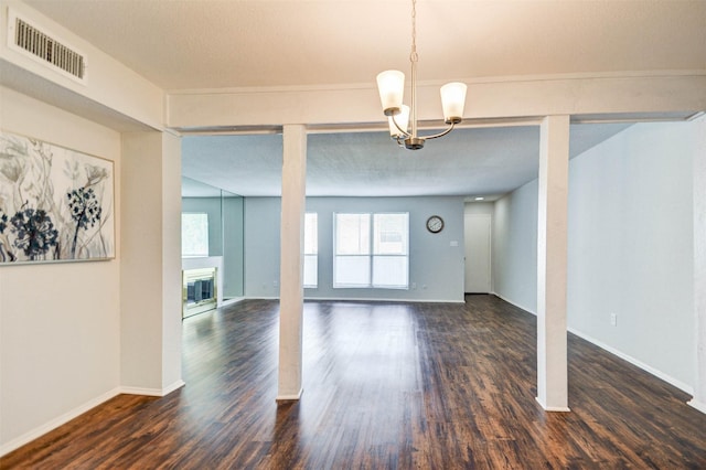 unfurnished dining area with visible vents, baseboards, a chandelier, wood finished floors, and a glass covered fireplace