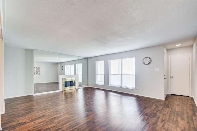 unfurnished living room featuring a glass covered fireplace, baseboards, a textured ceiling, and wood finished floors