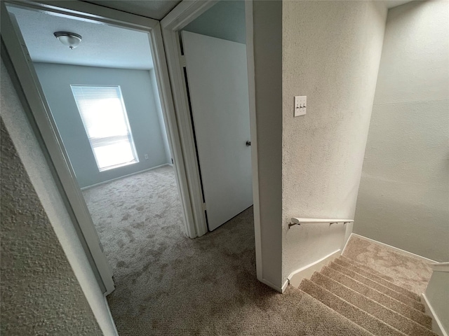 corridor featuring carpet flooring, a textured wall, baseboards, and stairs