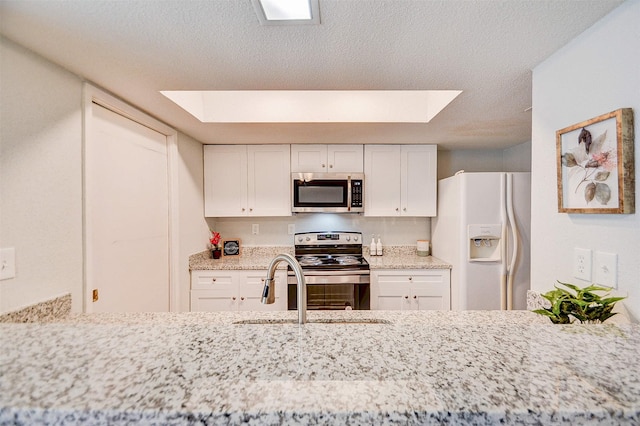 kitchen featuring a skylight, appliances with stainless steel finishes, white cabinetry, and light stone countertops
