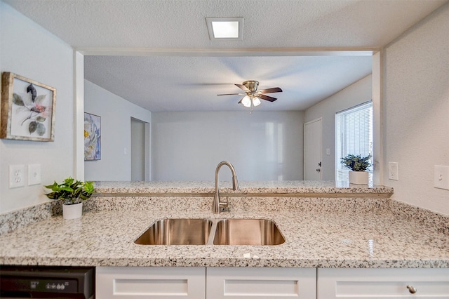 kitchen featuring light stone countertops, a ceiling fan, white cabinetry, dishwasher, and a sink