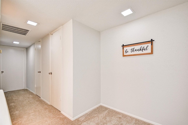 hallway with visible vents, light colored carpet, and baseboards