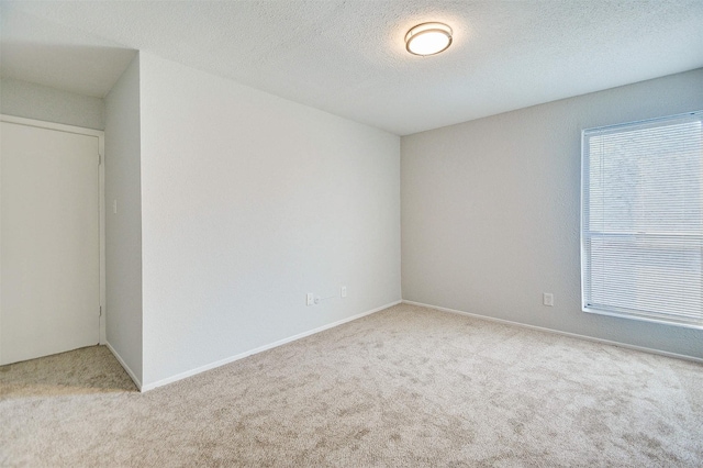 carpeted empty room featuring a textured ceiling and baseboards