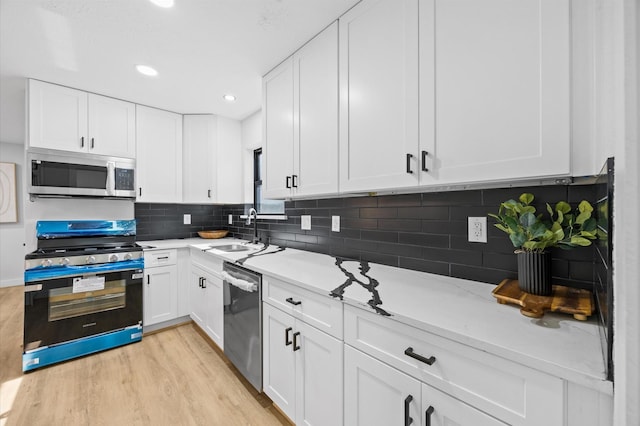 kitchen with light countertops, white cabinets, stainless steel appliances, light wood finished floors, and a sink