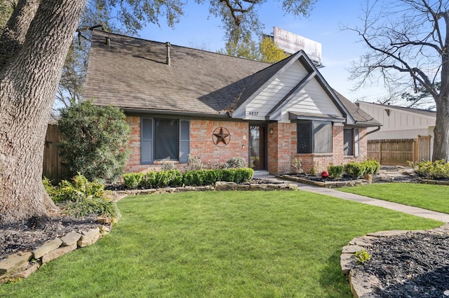 tudor house with a shingled roof, brick siding, fence, and a front lawn