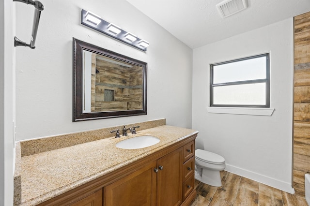bathroom featuring vanity, visible vents, toilet, wood finished floors, and baseboards