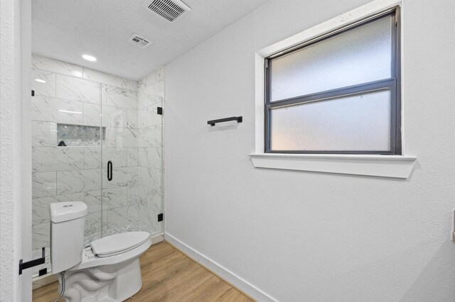 bathroom with baseboards, a marble finish shower, toilet, visible vents, and wood finished floors