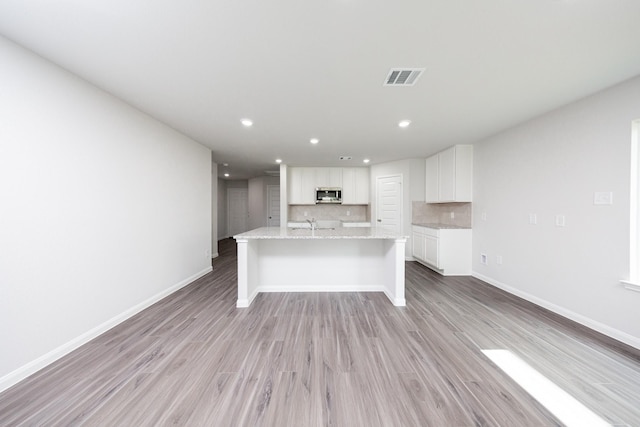 16547 Willow Forest Dr, Conroe, TX 77302 - kitchen featuring stainless steel microwave, a kitchen island with sink, decorative backsplash, white cabinetry, and light wood-style flooring
