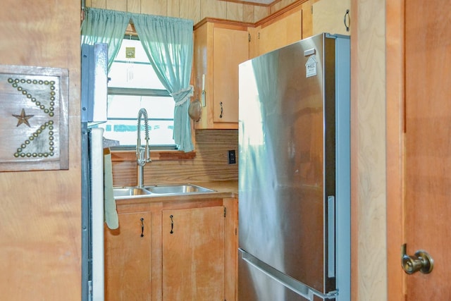 kitchen with light brown cabinets, light countertops, freestanding refrigerator, and a sink