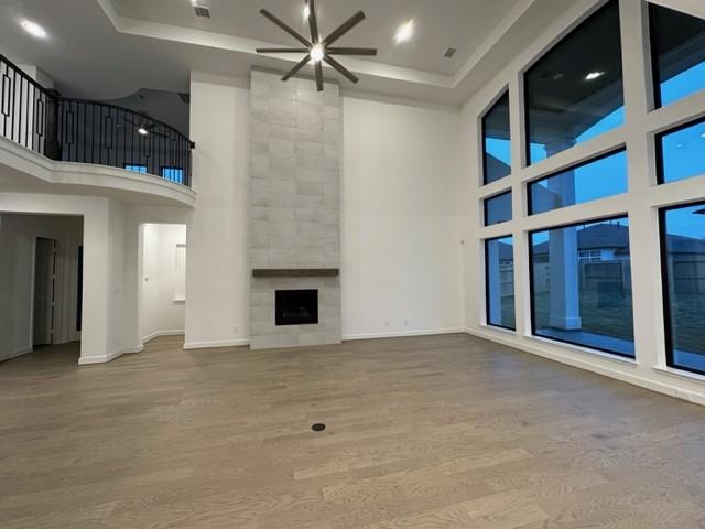 9015 Orchard Cv, Missouri City, TX 77459 - unfurnished living room with a raised ceiling, a high ceiling, ceiling fan, and wood finished floors