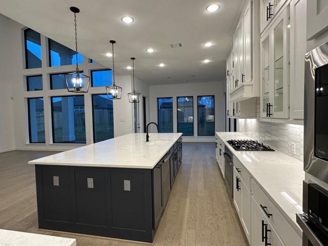 9015 Orchard Cv, Missouri City, TX 77459 - kitchen featuring recessed lighting, glass insert cabinets, white cabinetry, light wood finished floors, and a large island with sink