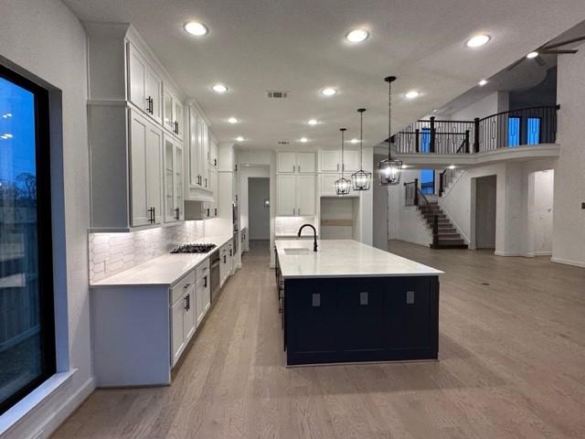9015 Orchard Cv, Missouri City, TX 77459 - kitchen with light countertops, white cabinetry, gas stovetop, a spacious island, and a sink