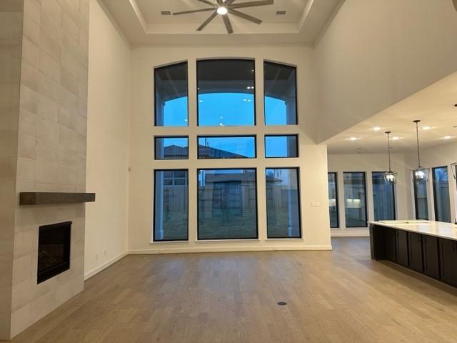 9015 Orchard Cv, Missouri City, TX 77459 - unfurnished living room with baseboards, a high ceiling, a tiled fireplace, ceiling fan, and wood finished floors