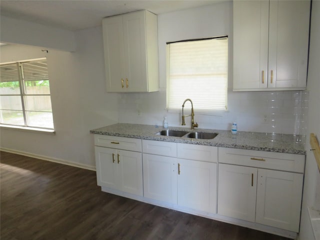 kitchen featuring a sink, decorative backsplash, light stone counters, and white cabinets