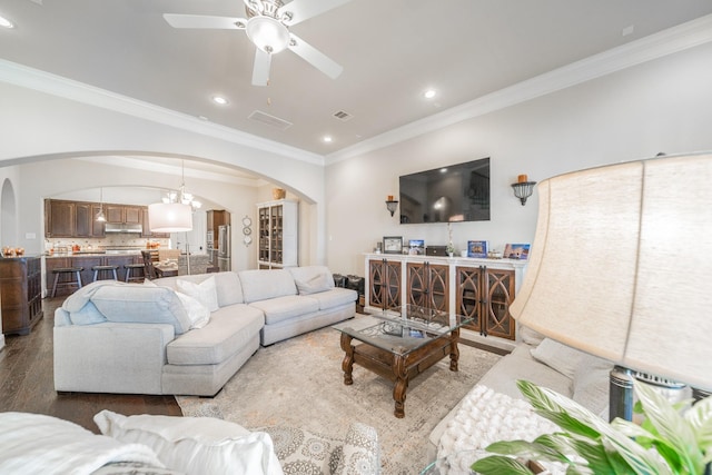 living room with crown molding, visible vents, arched walkways, wood finished floors, and ceiling fan with notable chandelier