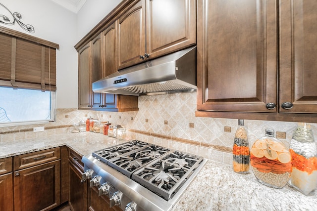 kitchen with dark brown cabinetry, tasteful backsplash, light stone countertops, stainless steel gas stovetop, and under cabinet range hood