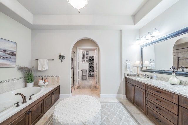 bathroom with a walk in closet, a bath, and vanity