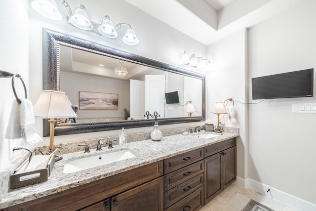 bathroom featuring double vanity, baseboards, a tray ceiling, and a sink
