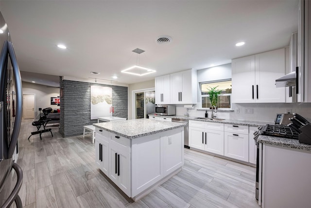 kitchen featuring a center island, light stone countertops, wall chimney exhaust hood, appliances with stainless steel finishes, and a sink