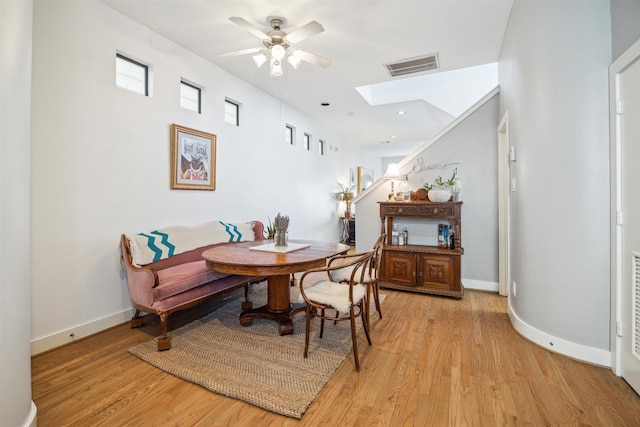 dining space with a skylight, light wood finished floors, a ceiling fan, and visible vents