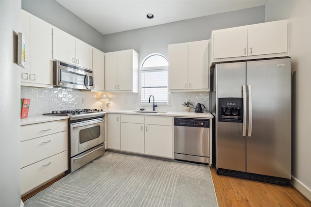 kitchen featuring light wood-type flooring, light countertops, backsplash, appliances with stainless steel finishes, and a sink