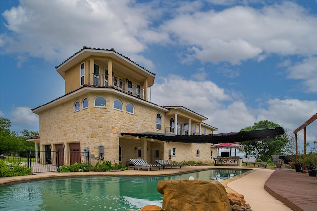 rear view of property featuring a fenced in pool, a patio, a balcony, stone siding, and fence