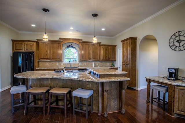 kitchen with a large island, baseboards, arched walkways, freestanding refrigerator, and a kitchen bar