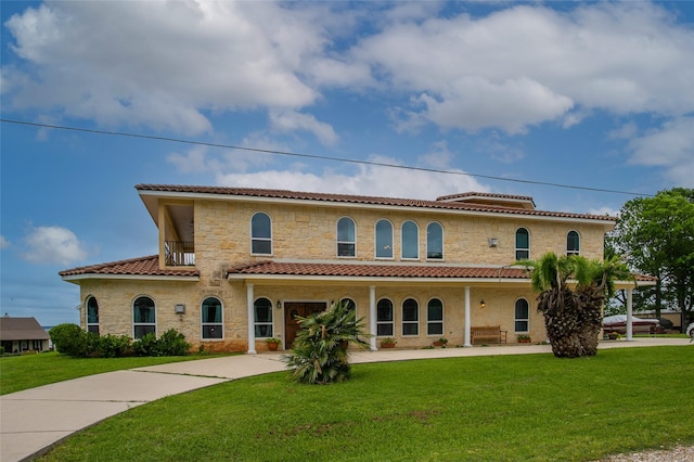 mediterranean / spanish house with concrete driveway, a tile roof, stone siding, and a front lawn